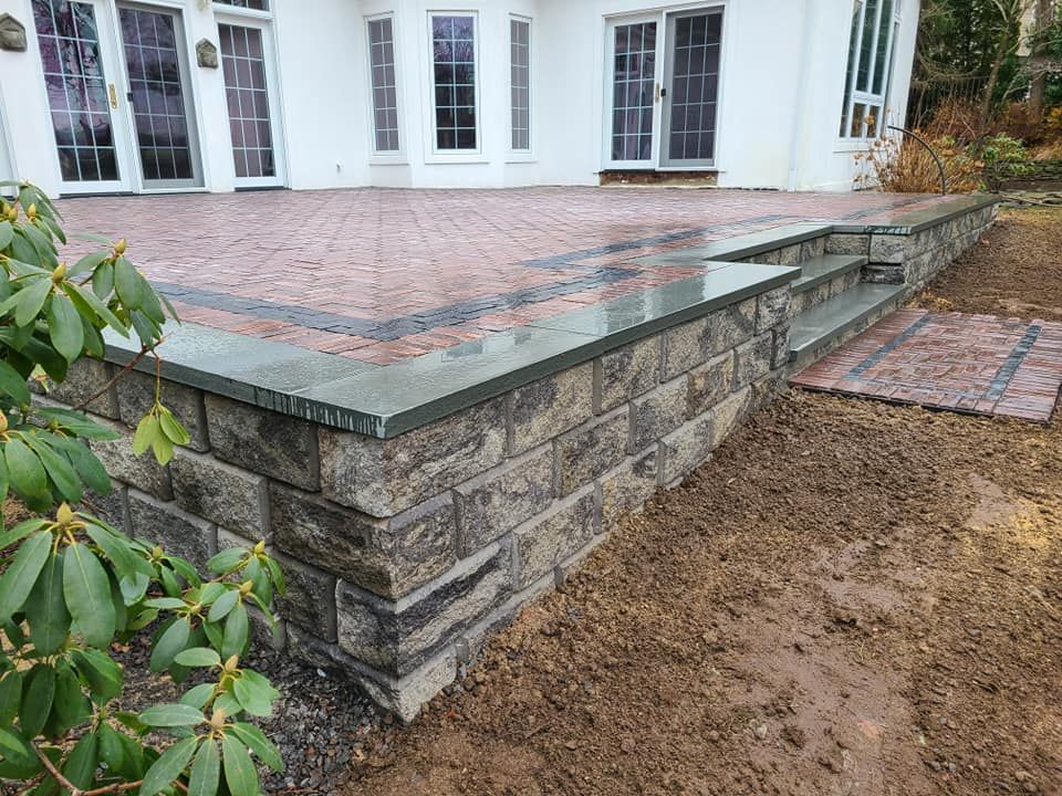 Brick patio with retaining wall and steps leading to a house with glass doors.