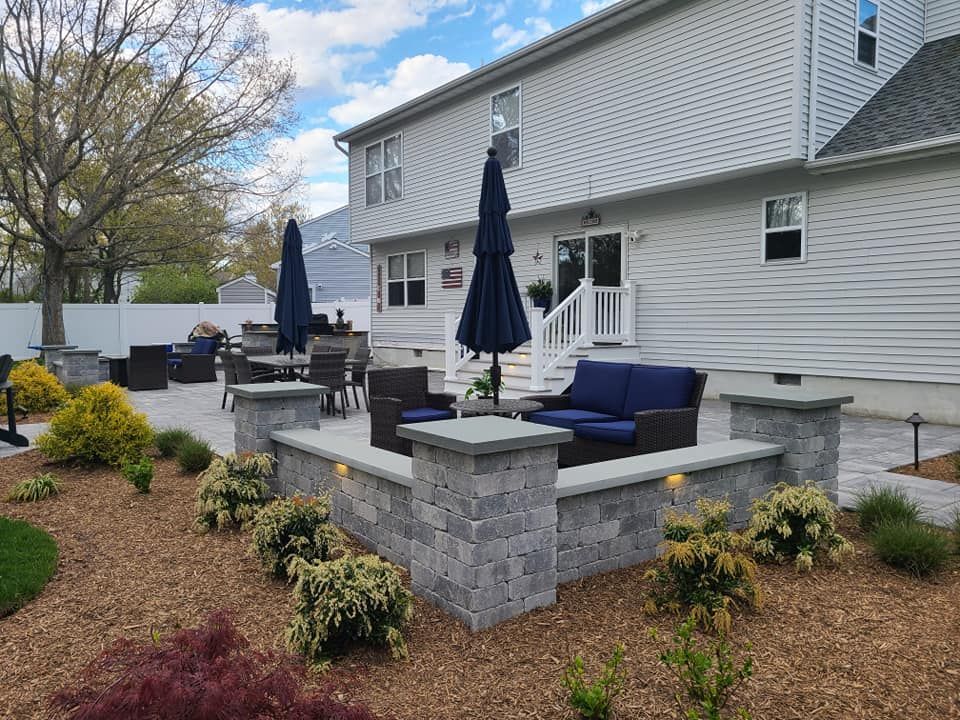 Backyard patio with seating, umbrellas, and built-in planters with flowers, adjacent to a two-story house.
