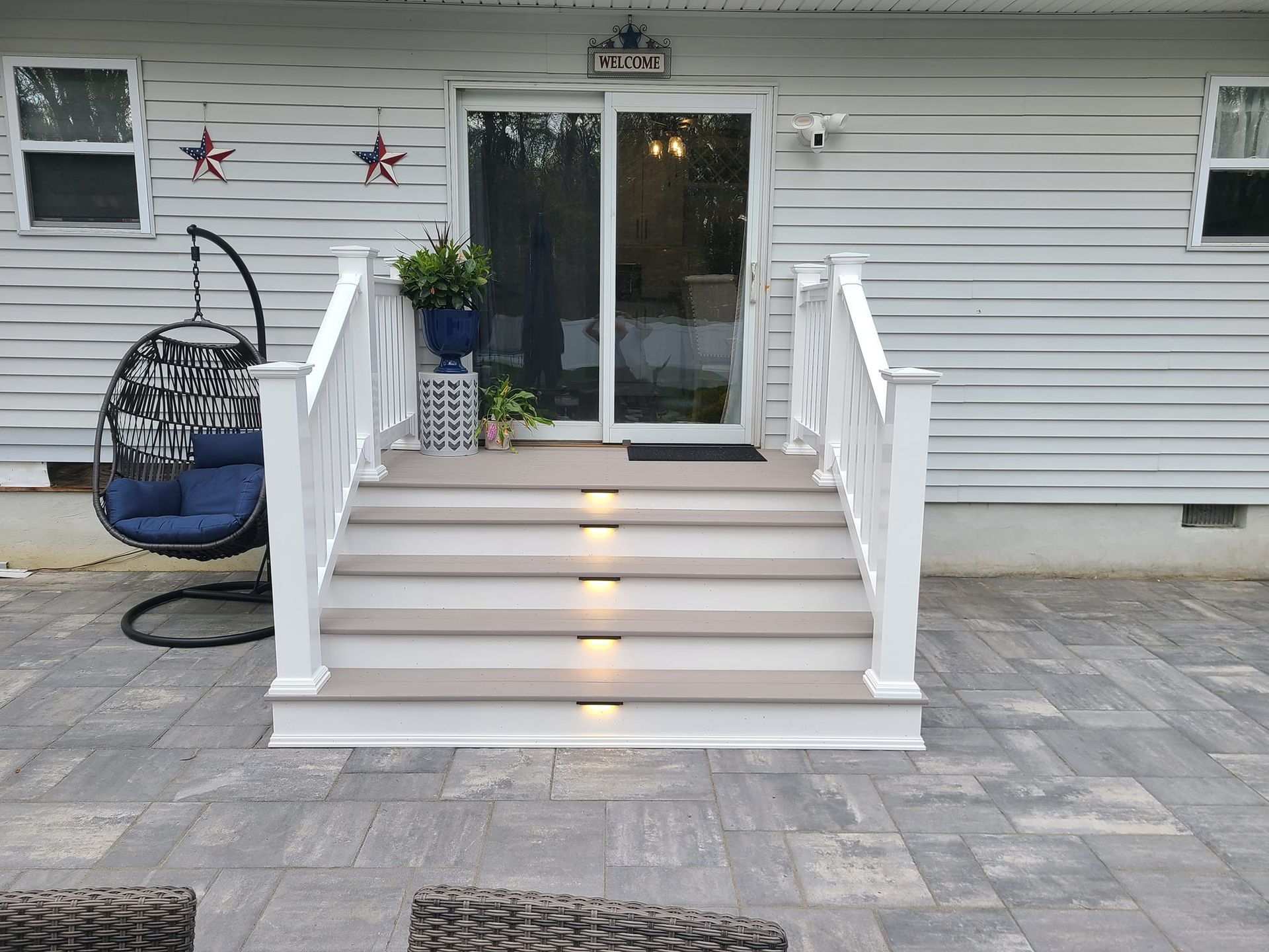 Gray steps with built-in lights leading to a sliding glass door. White railings and patio furniture.