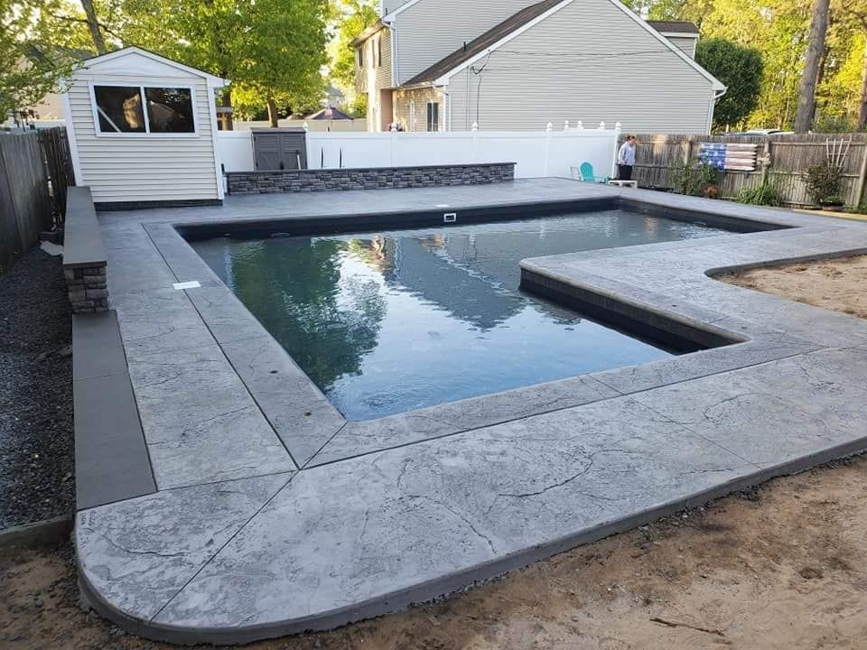 Concrete pool with stamped border, small shed, and backyard setting.