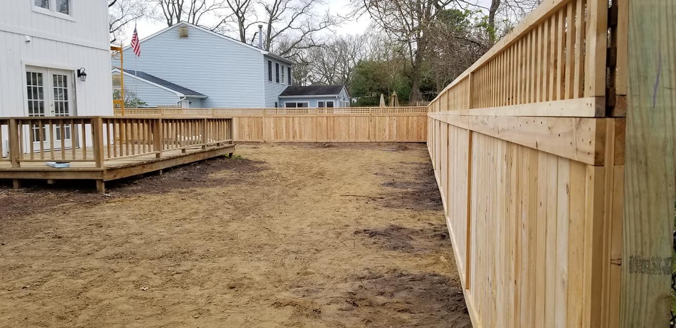 Backyard with new wooden fence and deck. Brown yard, houses in background.