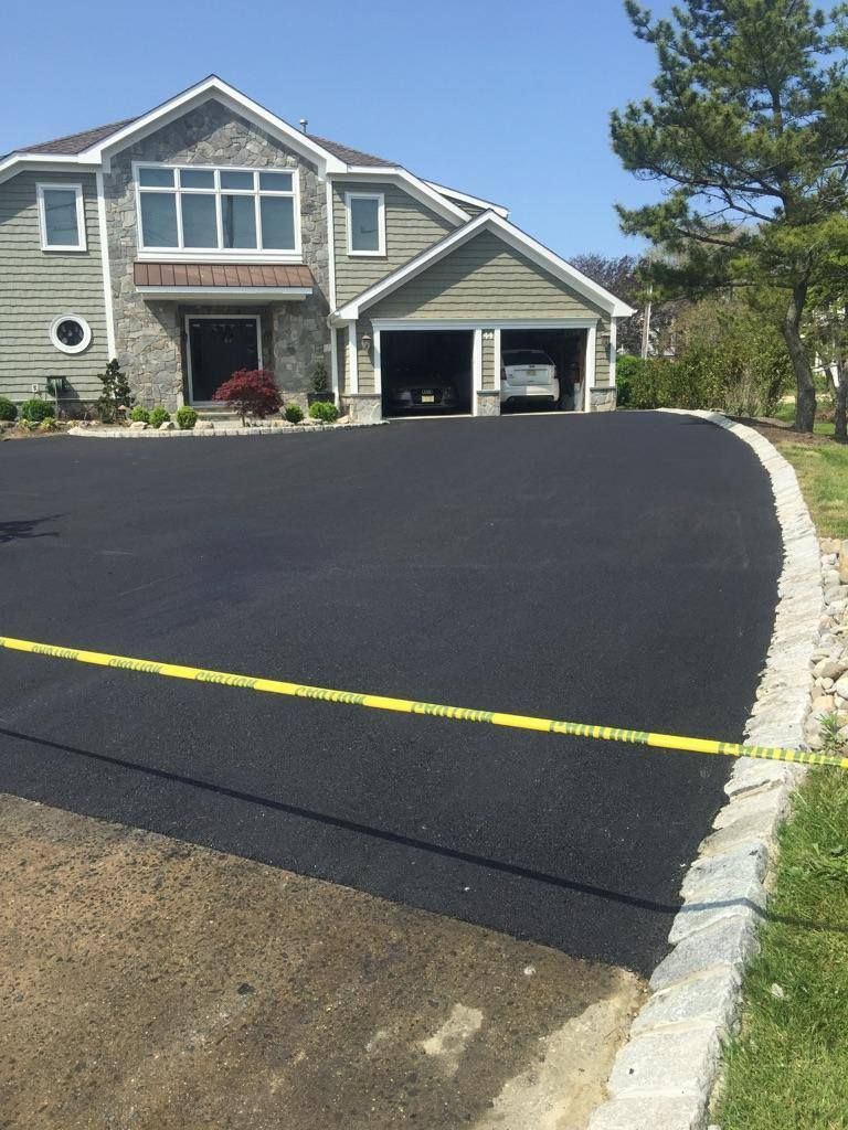 Newly paved black asphalt driveway in front of a light-green house with a two-car garage.