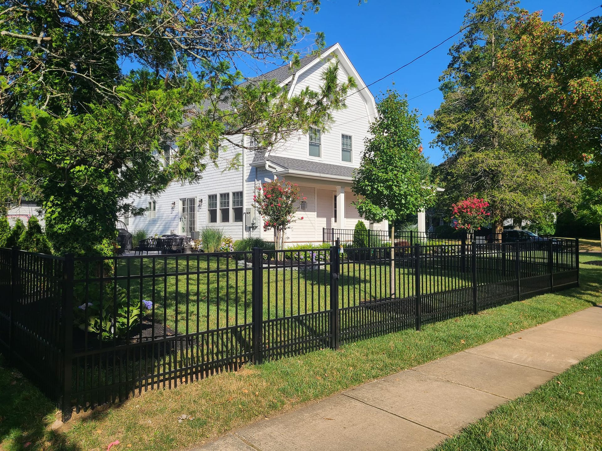 White house with black fence and trees on a sunny day.