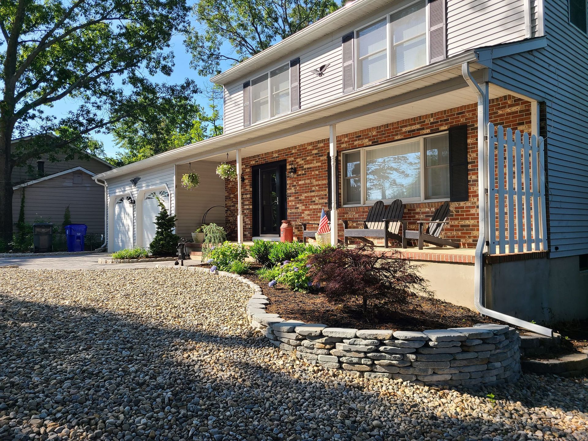 Two-story house with stone-lined flower bed, gravel drive, and white porch railing.