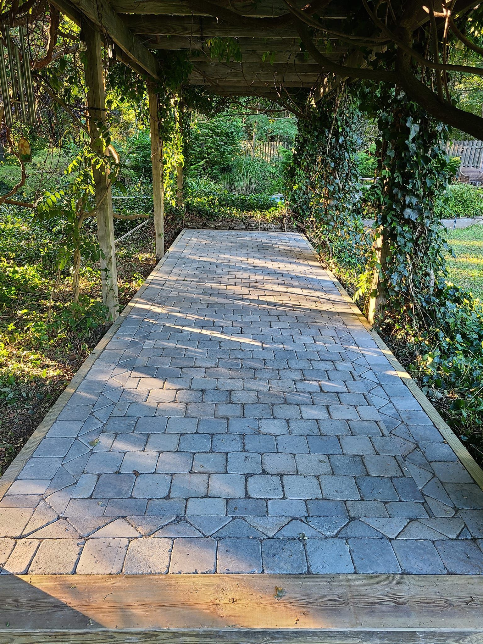 Stone path under a wooden trellis, with vines growing on the sides.