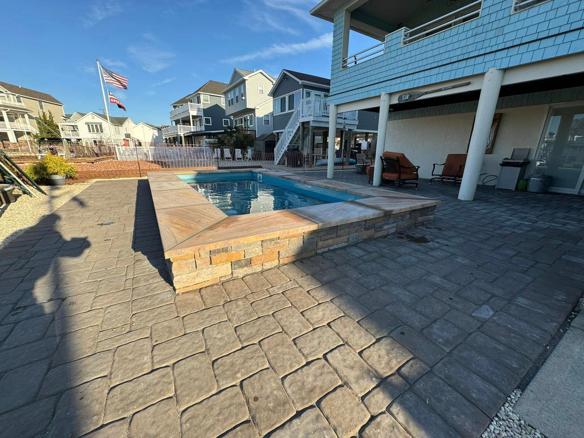 A pool patio with a brick border, blue pool, and waterfront house on a sunny day.