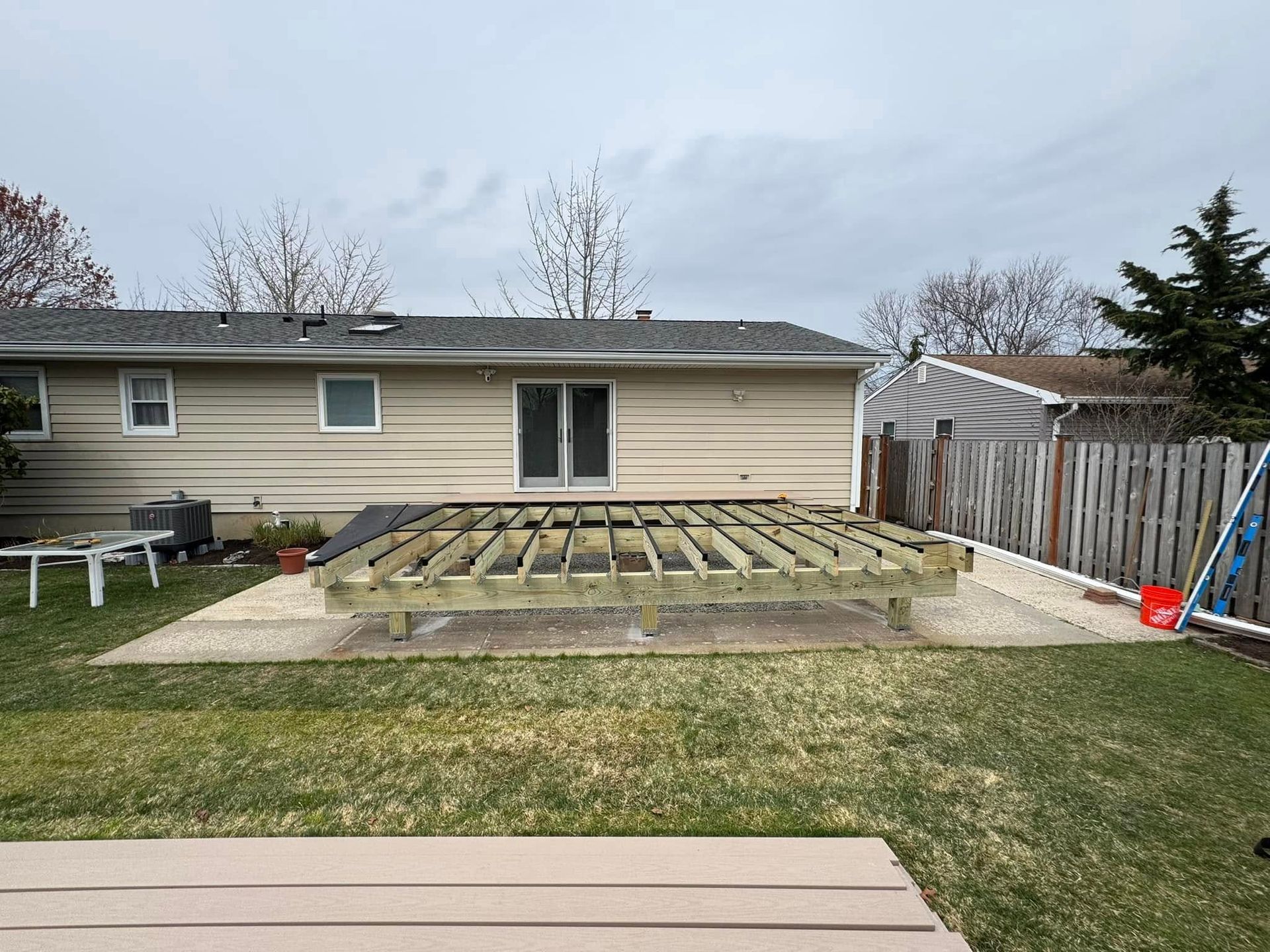 Backyard with a partially built wooden deck near a house with a sliding glass door. Overcast sky.