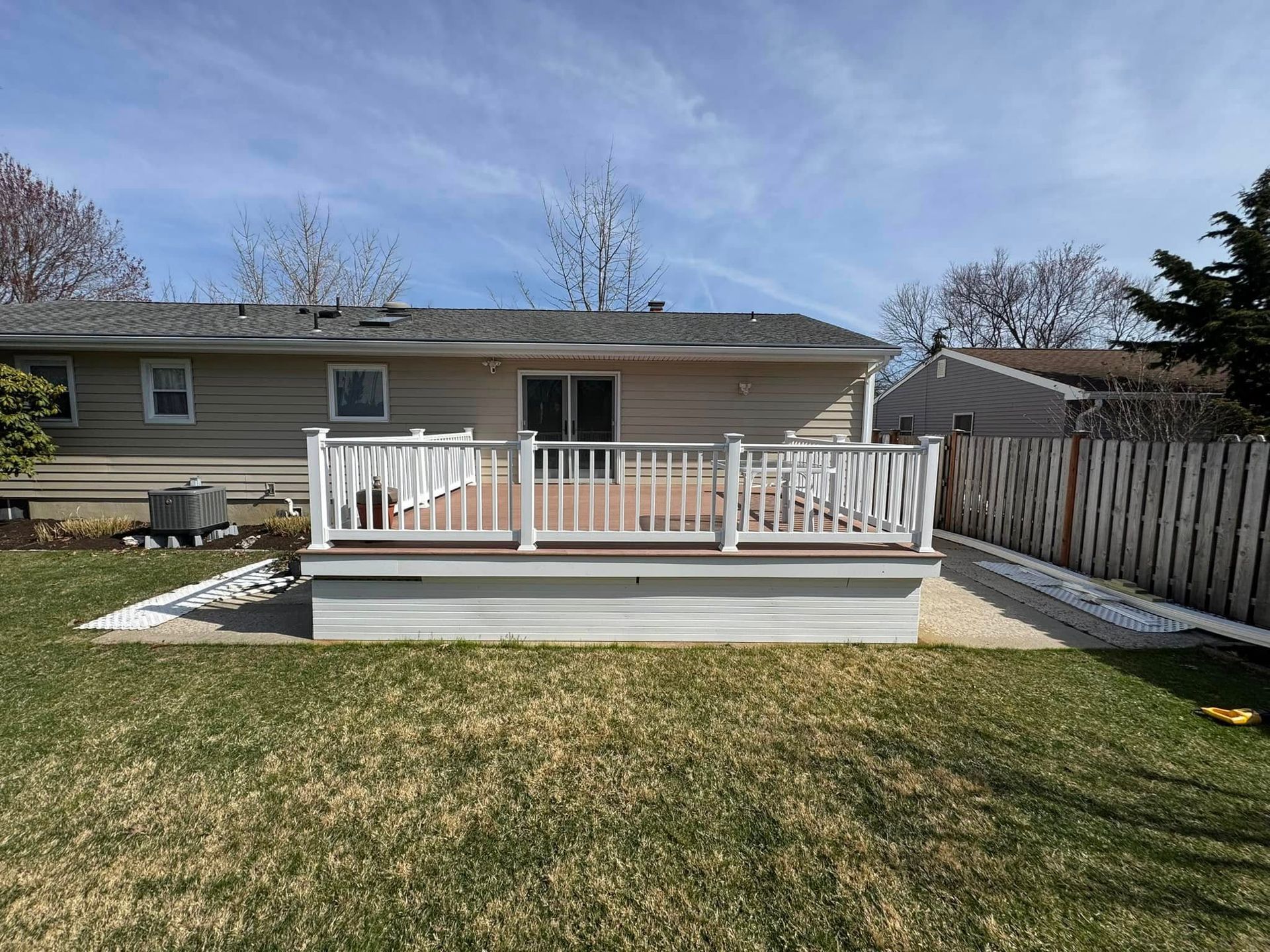 Backyard deck with white railing against a light-colored house. Brown deck boards, green grass.
