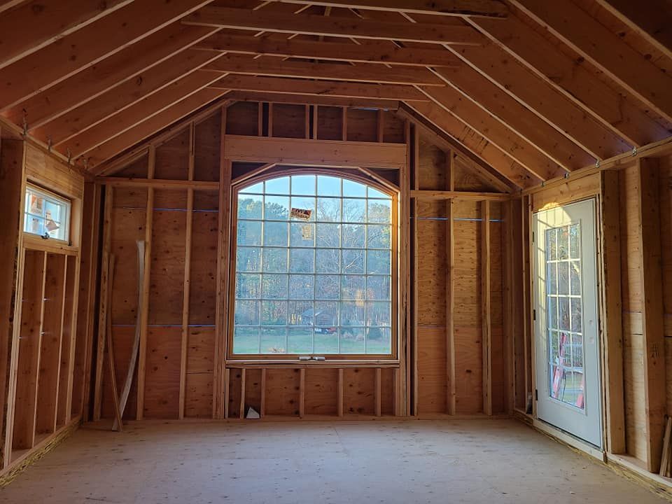 Interior of a wooden framed room with large arched window and door, natural light, under construction.