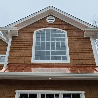 Brown shingled house exterior with a large arched window and copper-colored roofing. White trim and gutters.