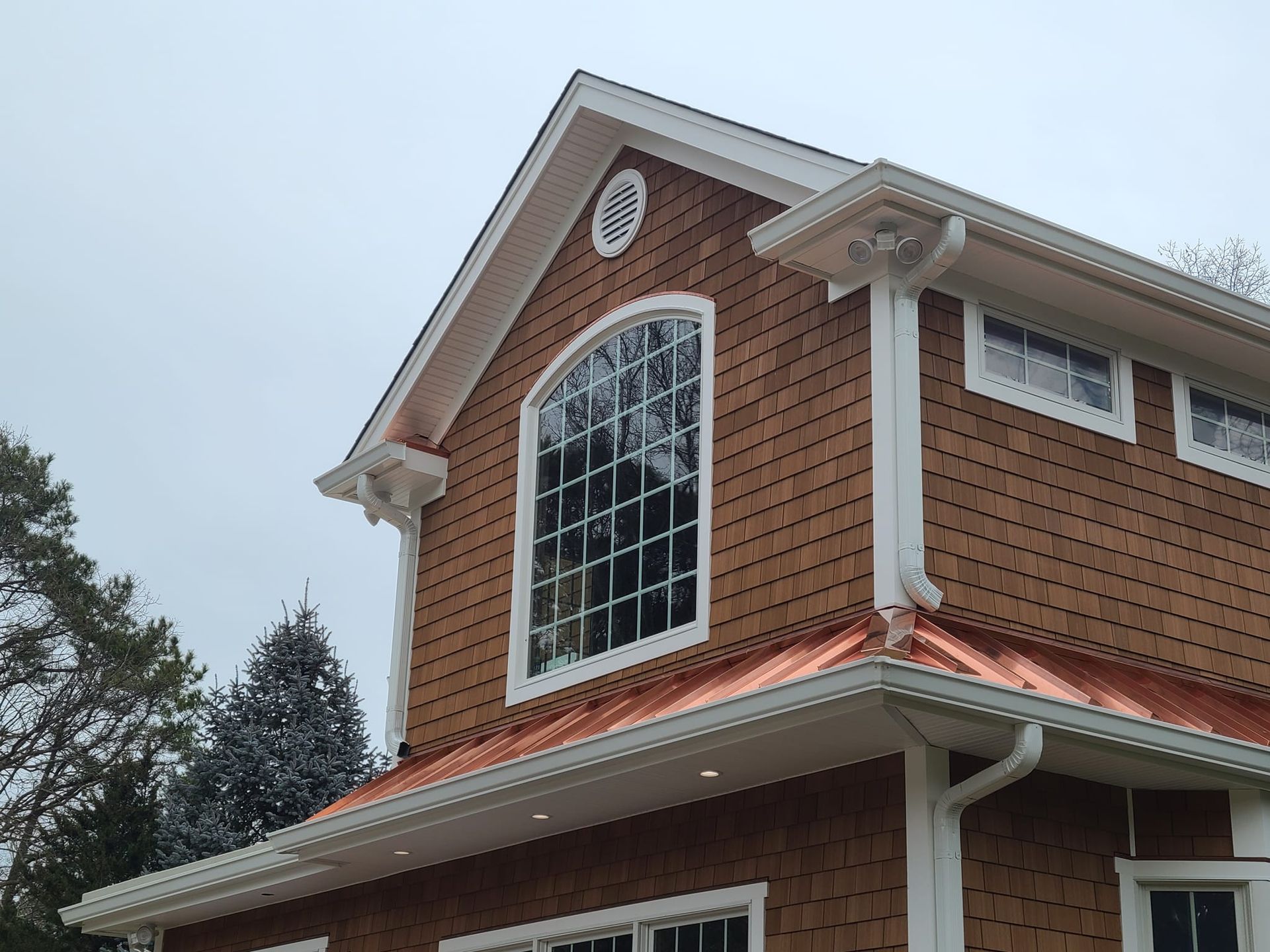 Brown shingle house with a copper roof, white trim, and a large arched window.