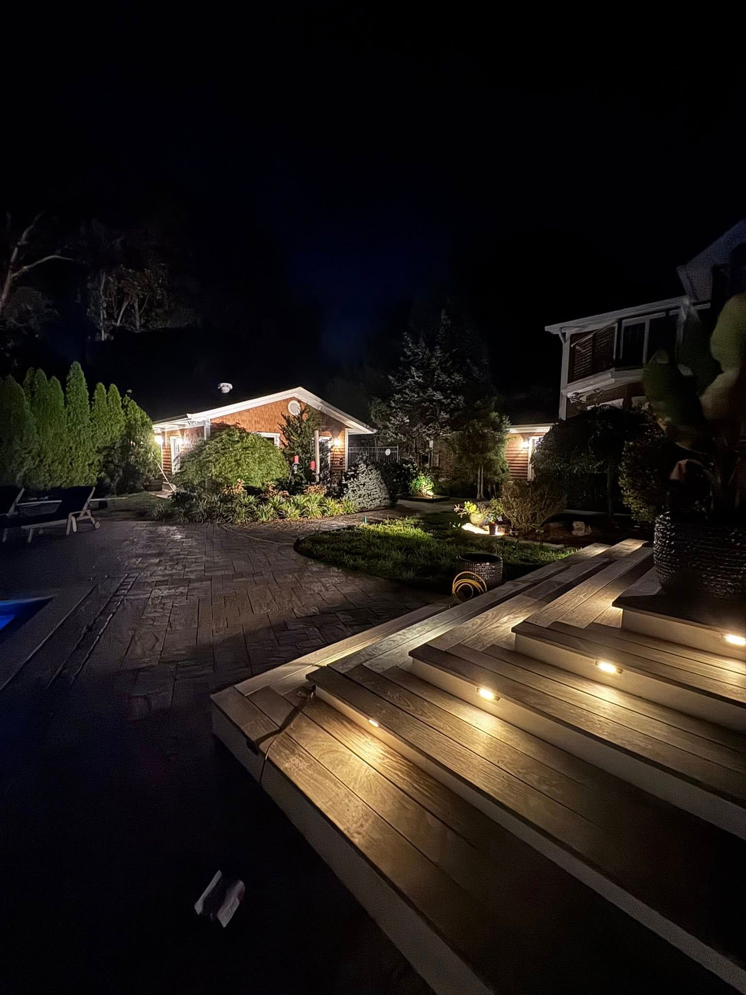 Night view of a lit backyard with a house, landscaping, and steps with lights.