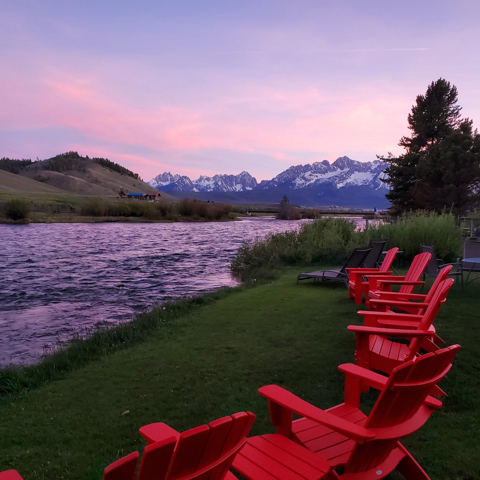 A row of red chairs sitting next to a river with mountains in the background