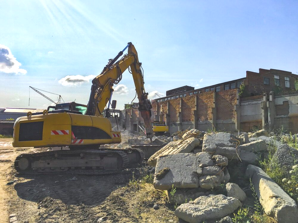 Yellow Excavator Demolishing a Brick Building on a Sunny Day — Dirt Werx in Batemans Bay, NSW