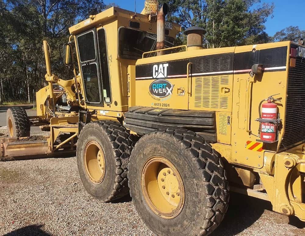 Yellow Caterpillar Grader on Gravel in an Outdoor Setting With Trees — Dirt Werx in Nowra, NSW