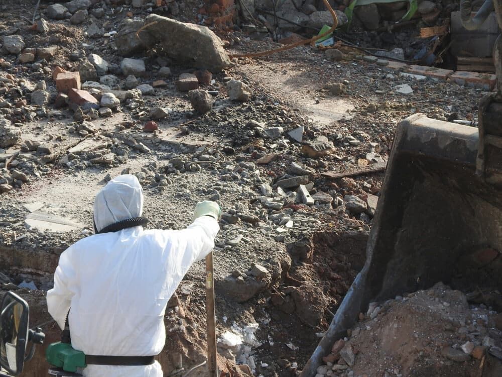 Person in White Protective Suit Digs in Rubble Next to Heavy Machinery — Dirt Werx in Batemans Bay, NSW
