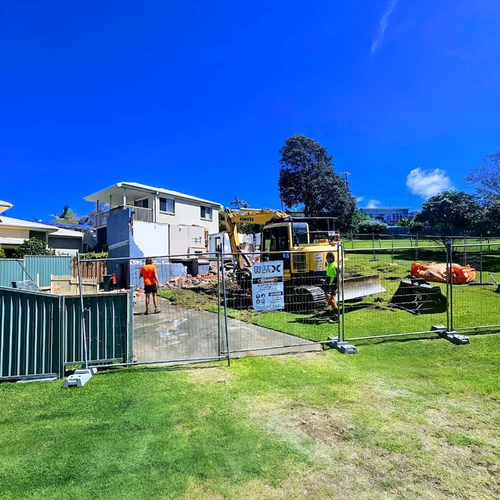 Construction site: excavator demolishing a house on a sunny day, workers present — Dirt Werx in Ulladulla, NSW