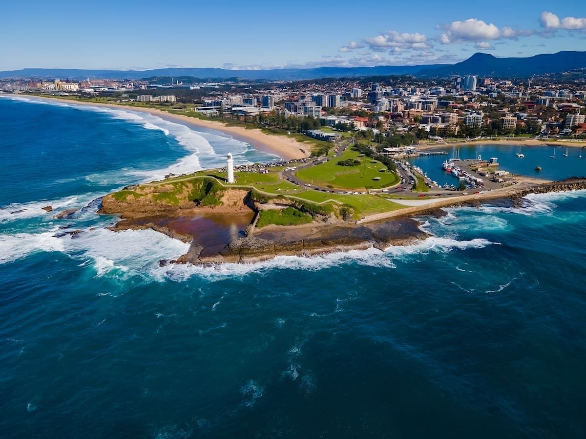 Coastal City View With Lighthouse on a Rocky Outcrop, Ocean Waves, Beach, and Buildings — Dirt Werx in Wollongong, NSW