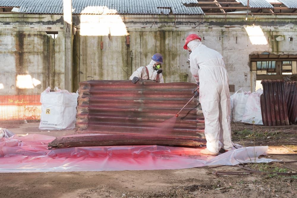 Two Workers in Protective Suits Spray Reddish Liquid on Corrugated Metal — Dirt Werx in Wollongong, NSW