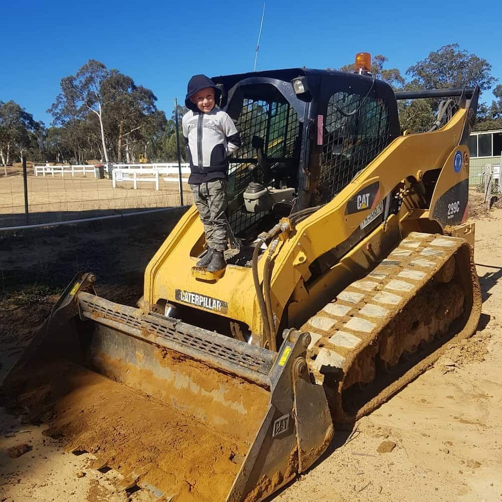 Young Child Standing on a Yellow Caterpillar Skid Steer Loader — Dirt Werx in Nowra, NSW