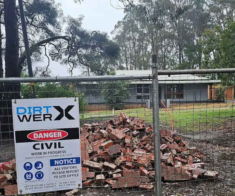 Demolished Brick Pile in Front of a Construction Site and a Safety Sign — Dirt Werx in Nowra, NSW