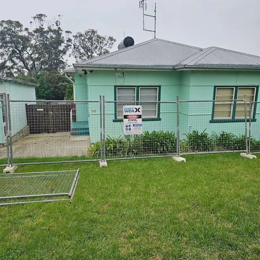 Green House Behind a Temporary Construction Fence on a Grassy Lawn — Dirt Werx in Nowra, NSW