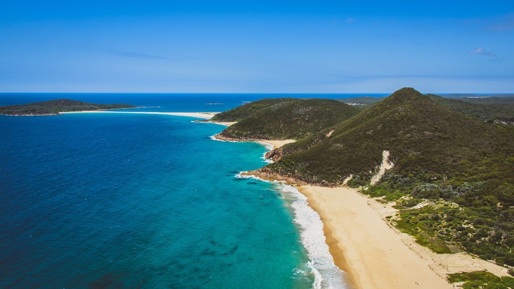 Aerial View Of A Turquoise Bay With A Sandy Beach, Green Hills — Dirt Werx in Port Stephens, NSW