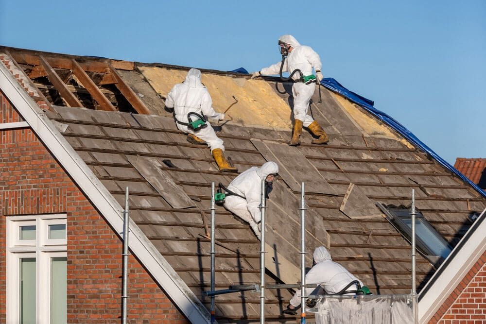 Four Workers in Hazmat Suits Removing an Old Roof From a Brick Building — Dirt Werx in Tathra, NSW