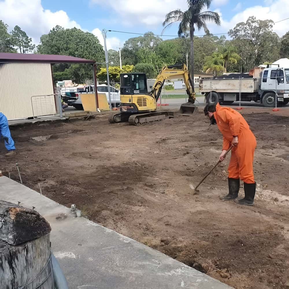 Construction Site: Person Rakes Dirt, Excavator, Dump Truck, and Building — Dirt Werx in Nowra, NSW