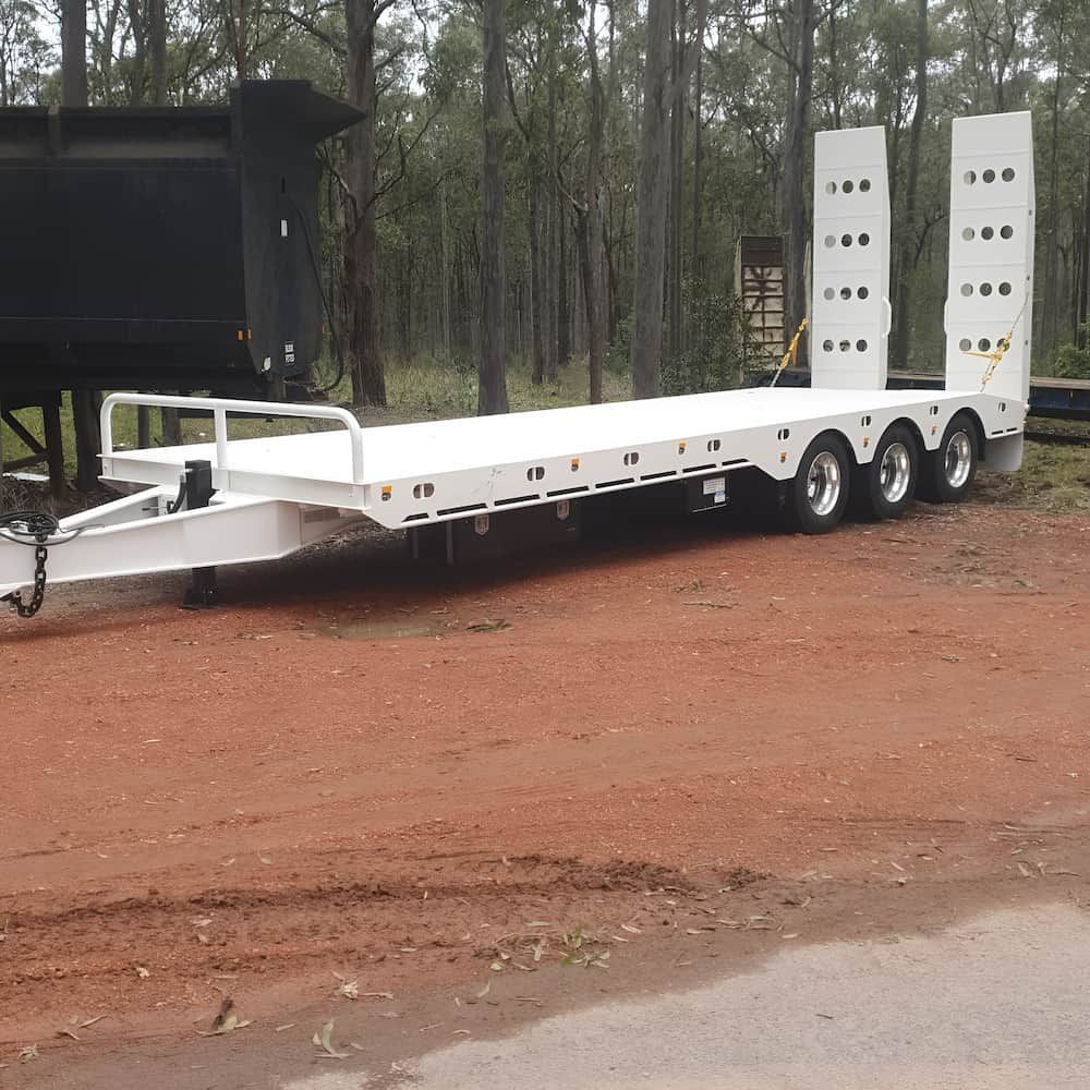 White Low-loader Trailer on Red Dirt Road, in Front of Forest Backdrop — Dirt Werx in Nowra, NSW