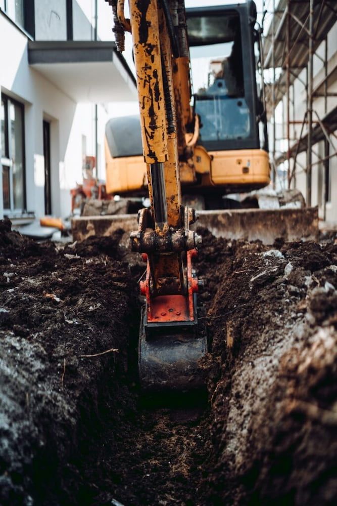 Yellow Excavator Digging a Trench in Front of a Building Under Construction — Dirt Werx in Merimbula, NSW