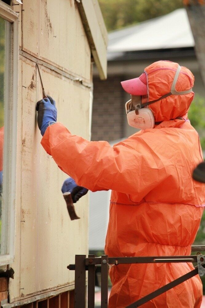 Person in Orange Hazmat Suit Scraping Exterior of Building With a Tool — Dirt Werx in Nowra, NSW