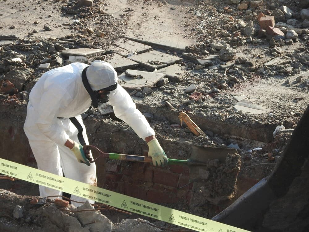 Person in Protective Suit Examining Debris With a Tool at a Construction Site — Dirt Werx in Narooma, NSW