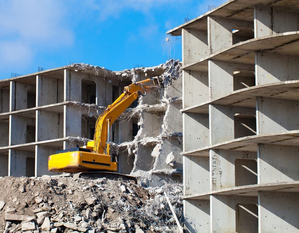 A Yellow Excavator Demolishes a Concrete Building Under a Blue Sky — Dirt Werx in Wollongong, NSW