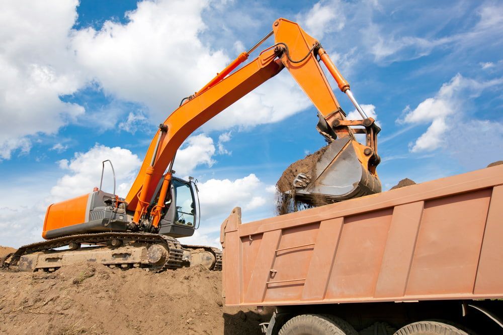 Orange Excavator Loading Dirt Into an Orange Dump Truck Against a Blue — Dirt Werx in Nowra, NSW