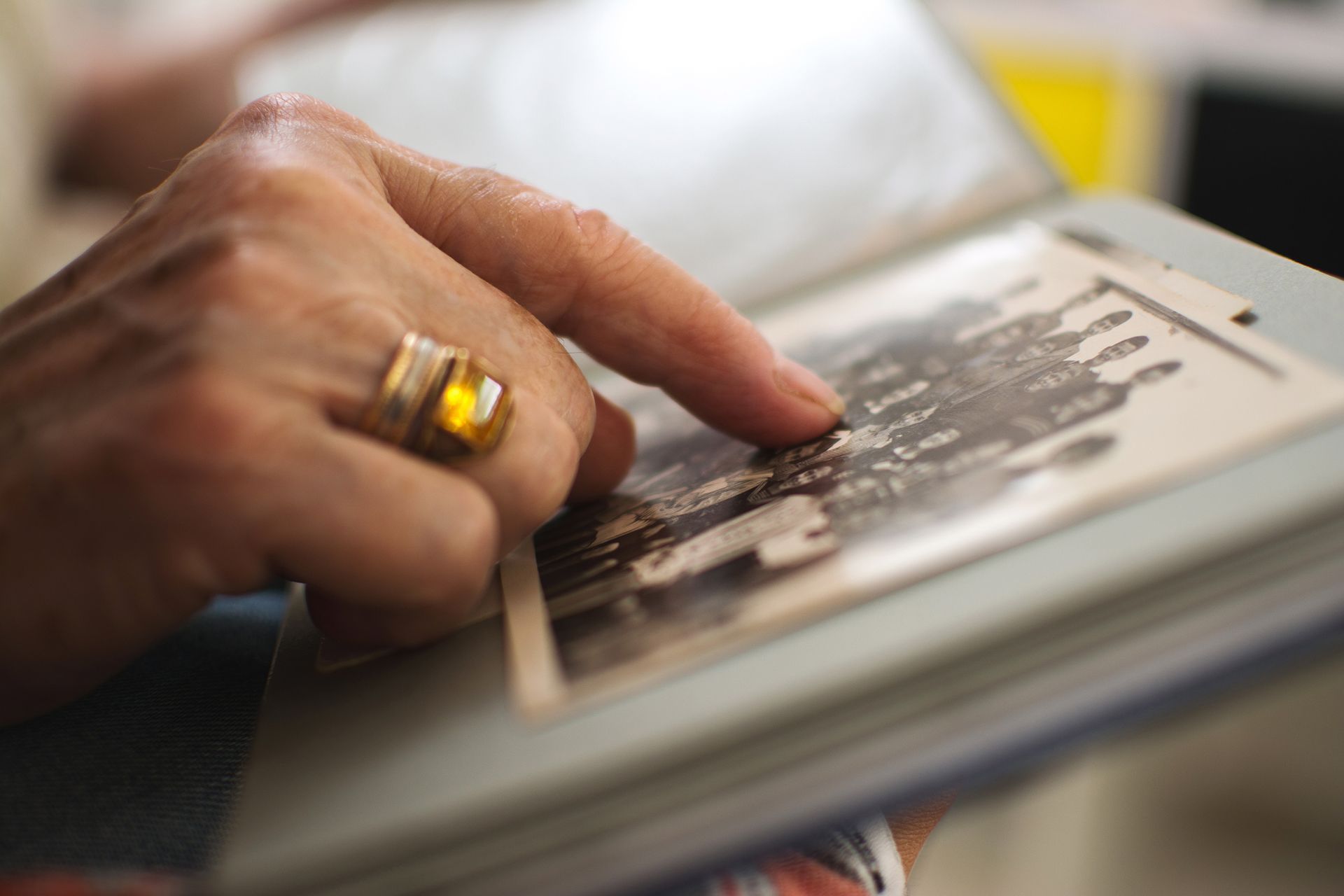 Hand pointing to a printed photo album page, with a gold ring visible.