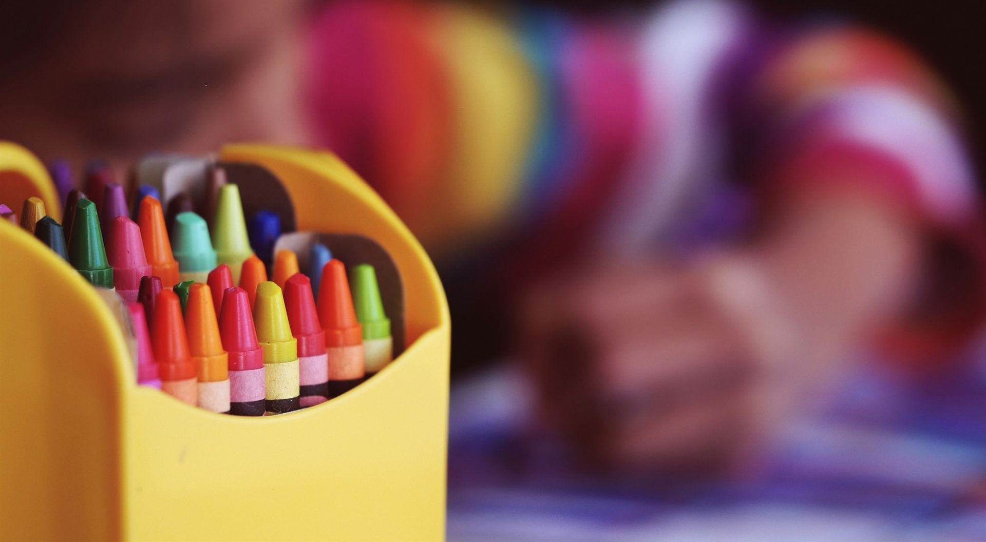A child is drawing with crayons in a yellow box.