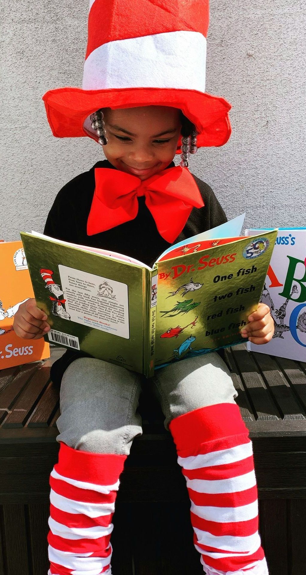 A little girl in a cat in the hat costume is reading a book.