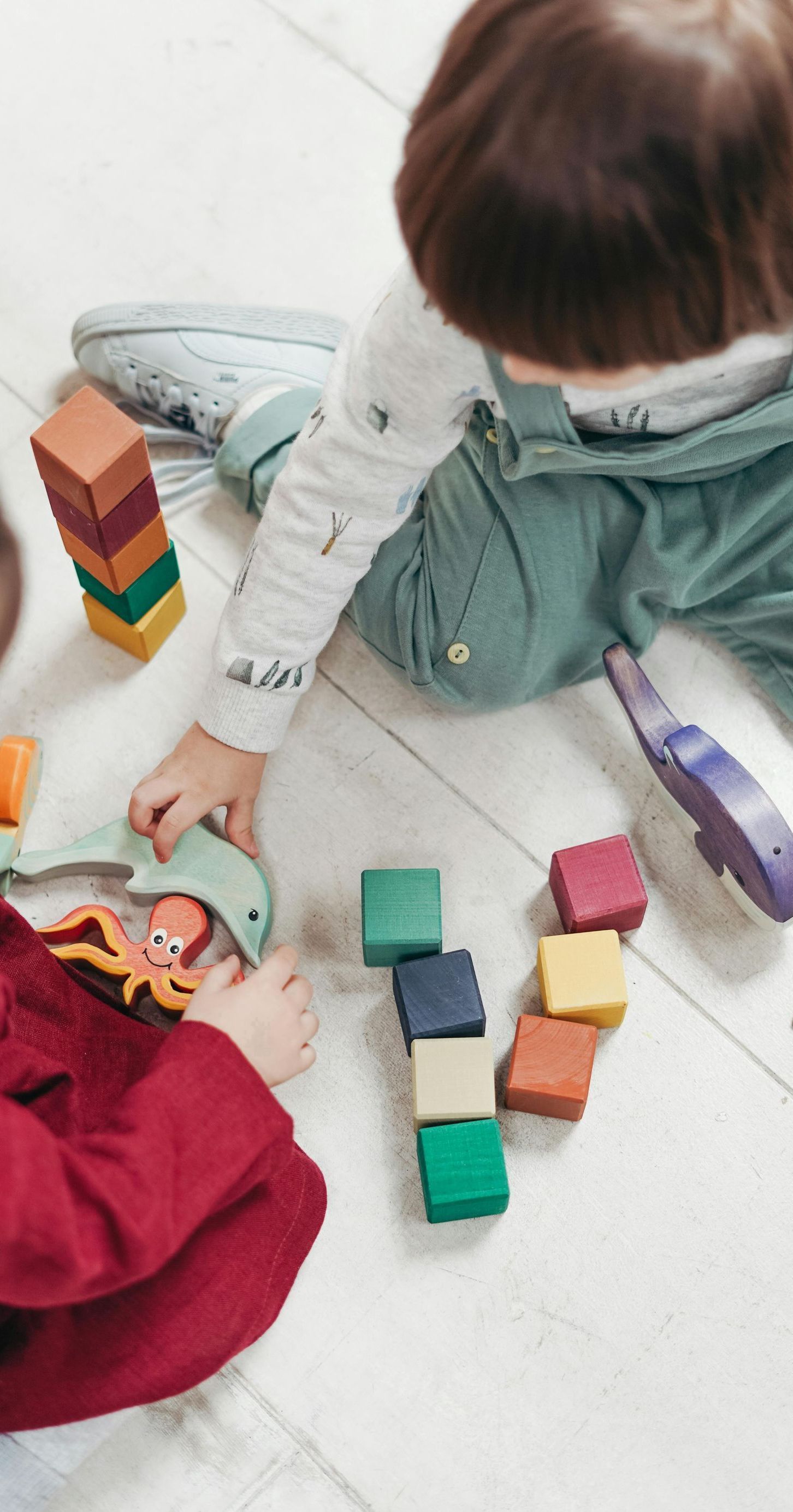 Two children are playing with wooden blocks on the floor.