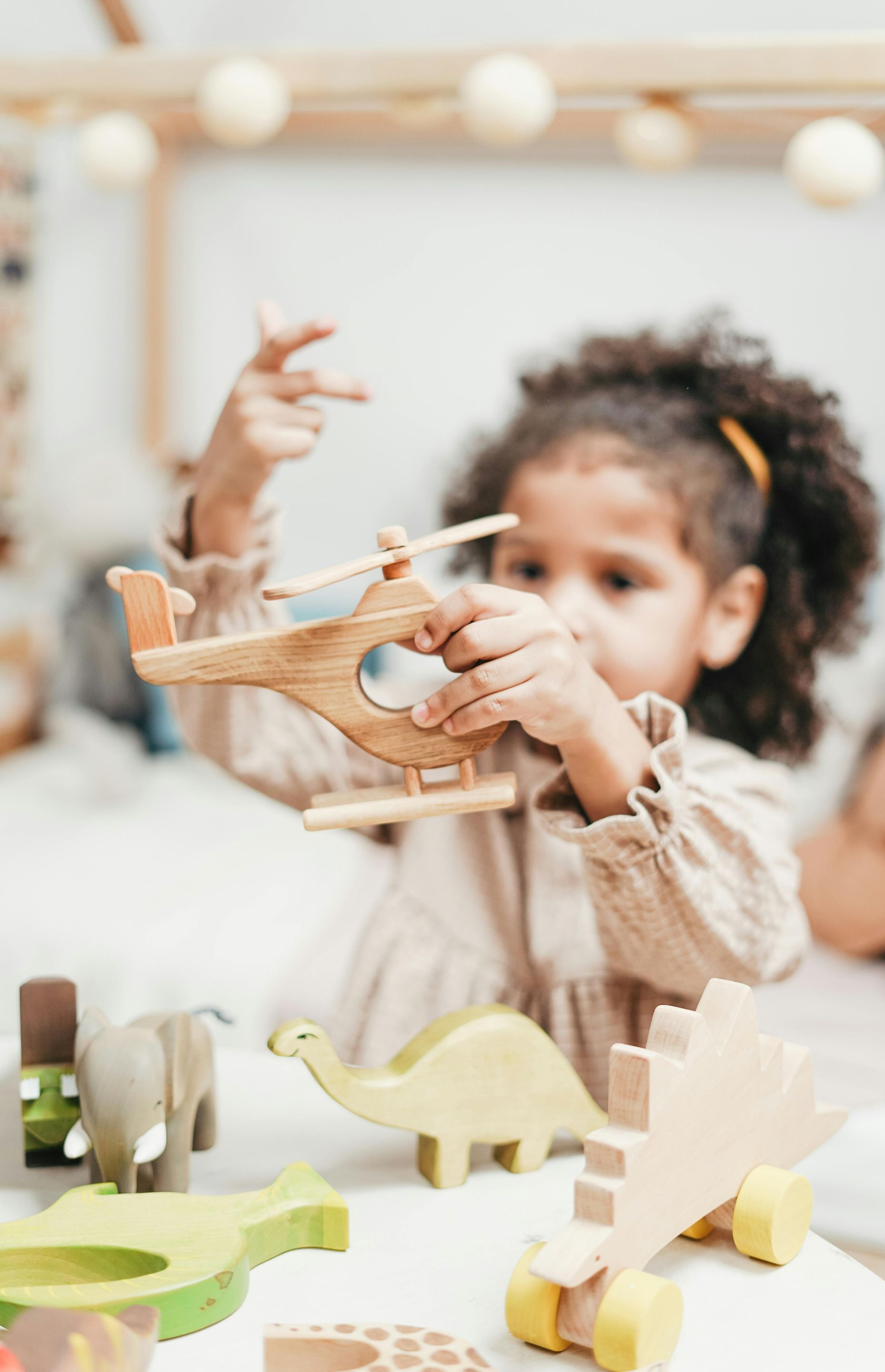 A little girl is playing with a wooden helicopter.