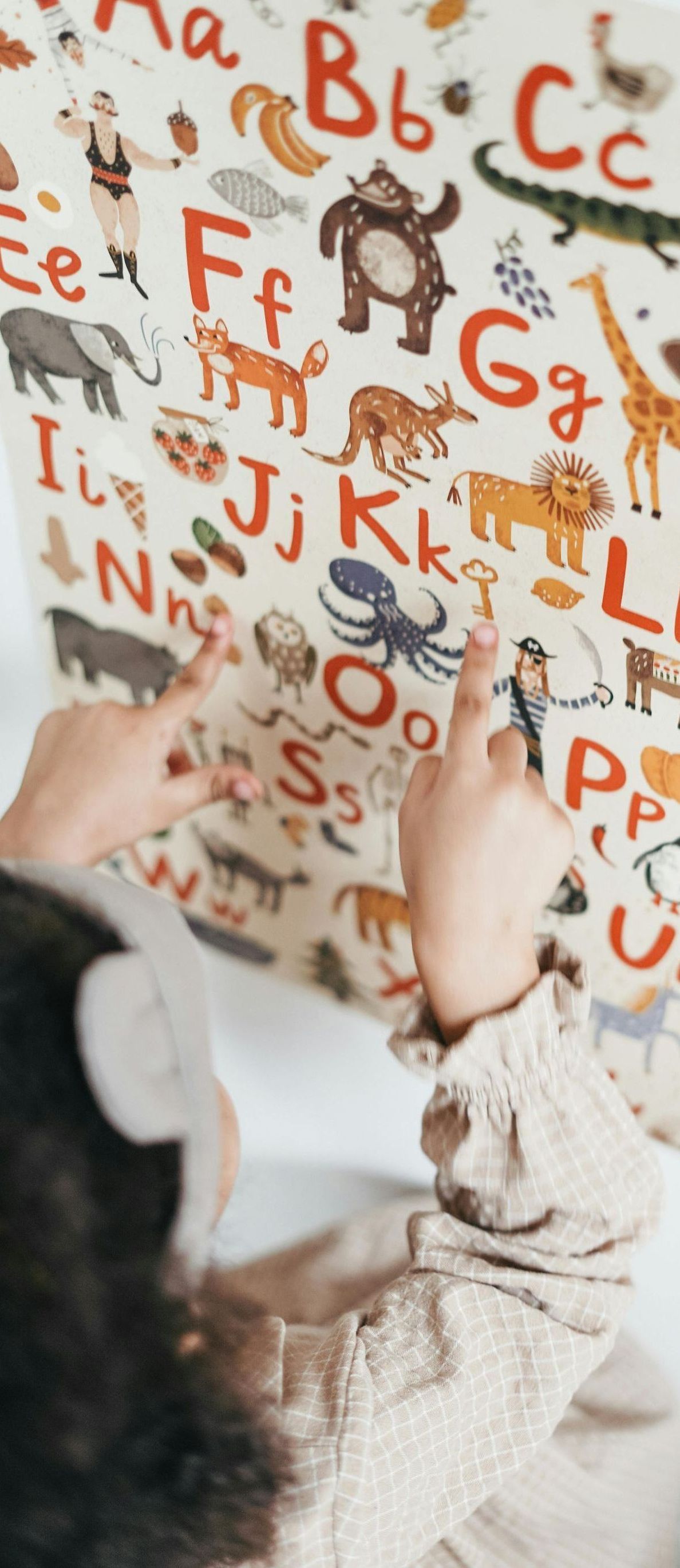 A child is playing with an alphabet poster on a wall.