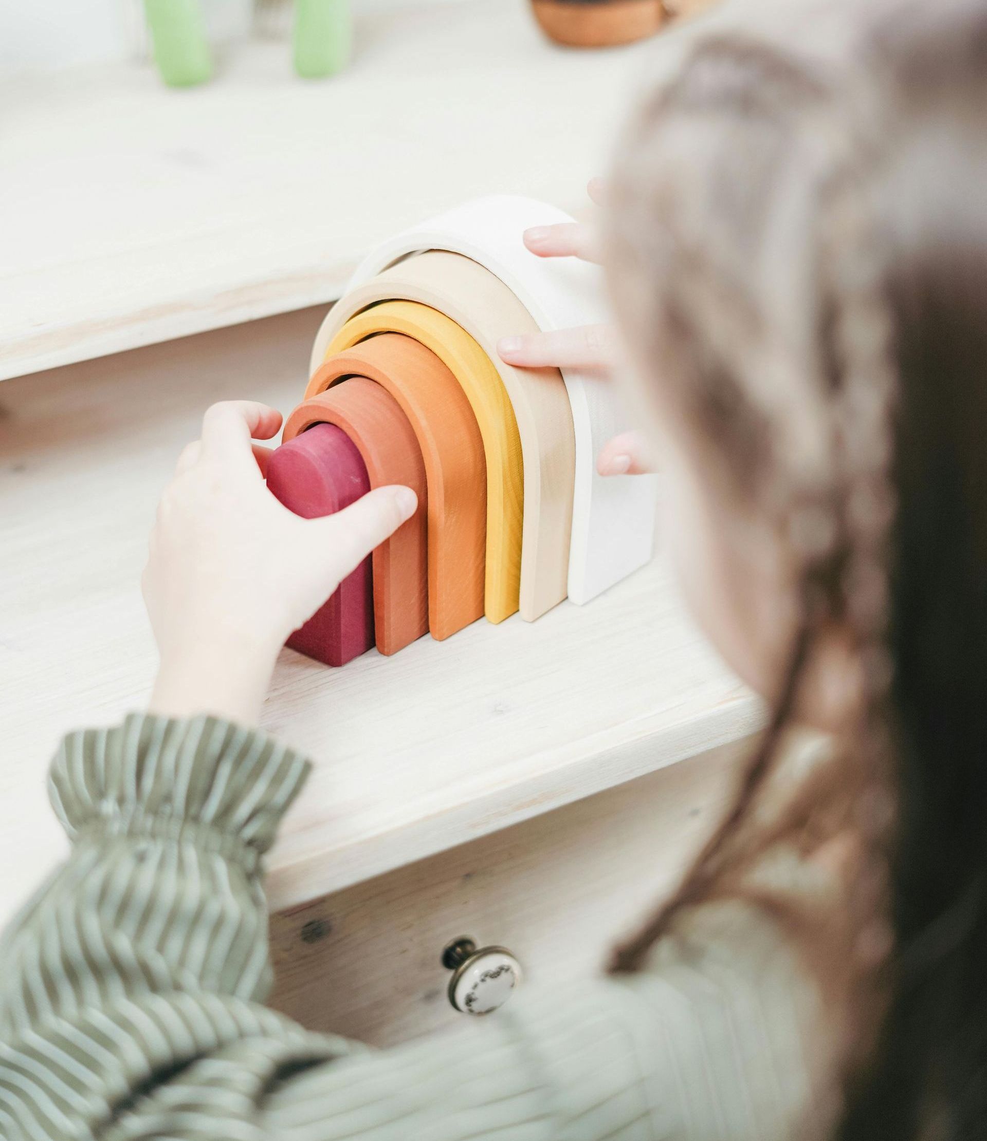 A child is playing with a wooden rainbow stacker