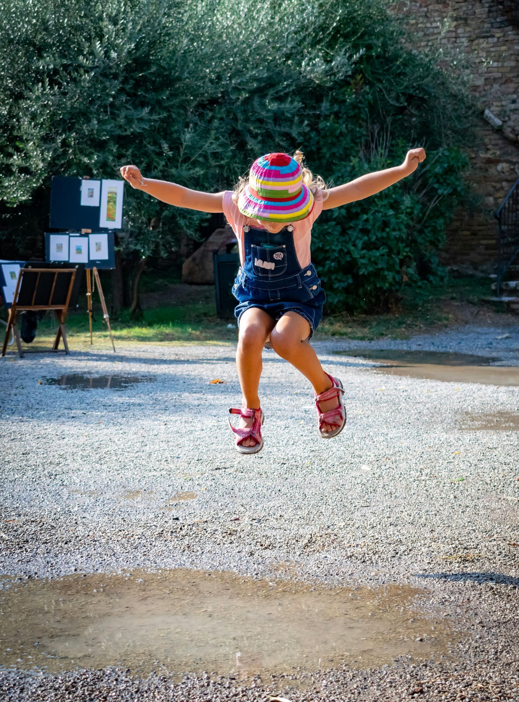 A little girl is jumping in the air with her arms outstretched.