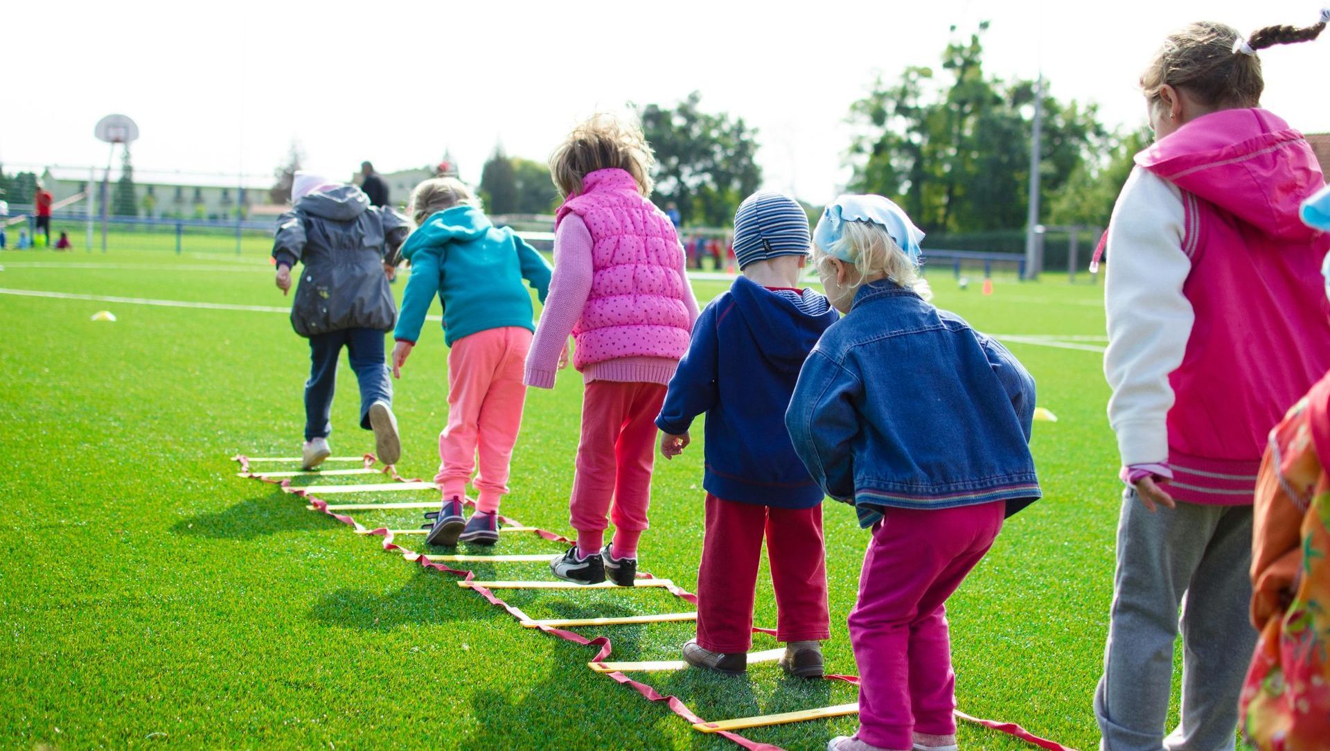 A group of children are walking across a ladder on a field.