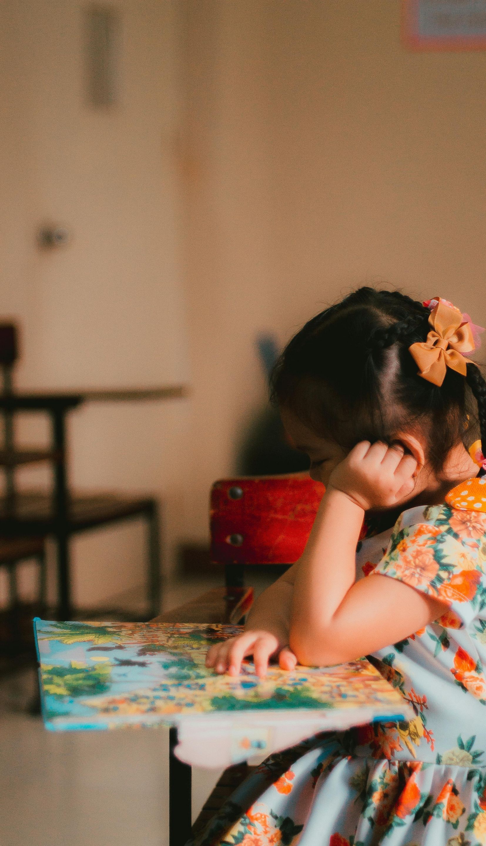 A little girl is sitting at a desk reading a book.