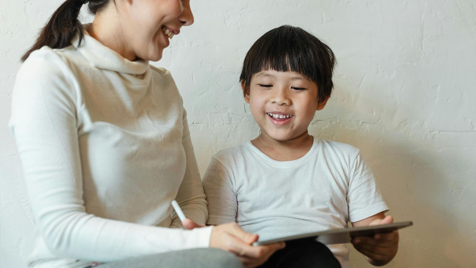A woman and a child are sitting on the floor looking at a tablet.