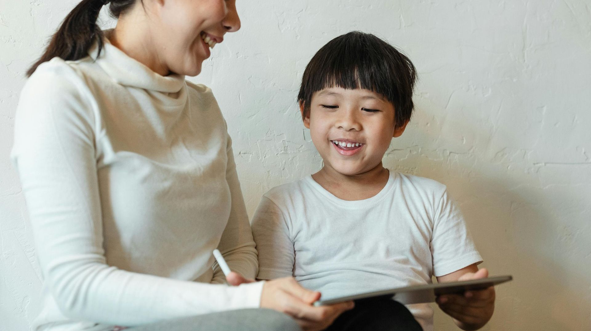 A woman and a child are sitting next to each other looking at a tablet.