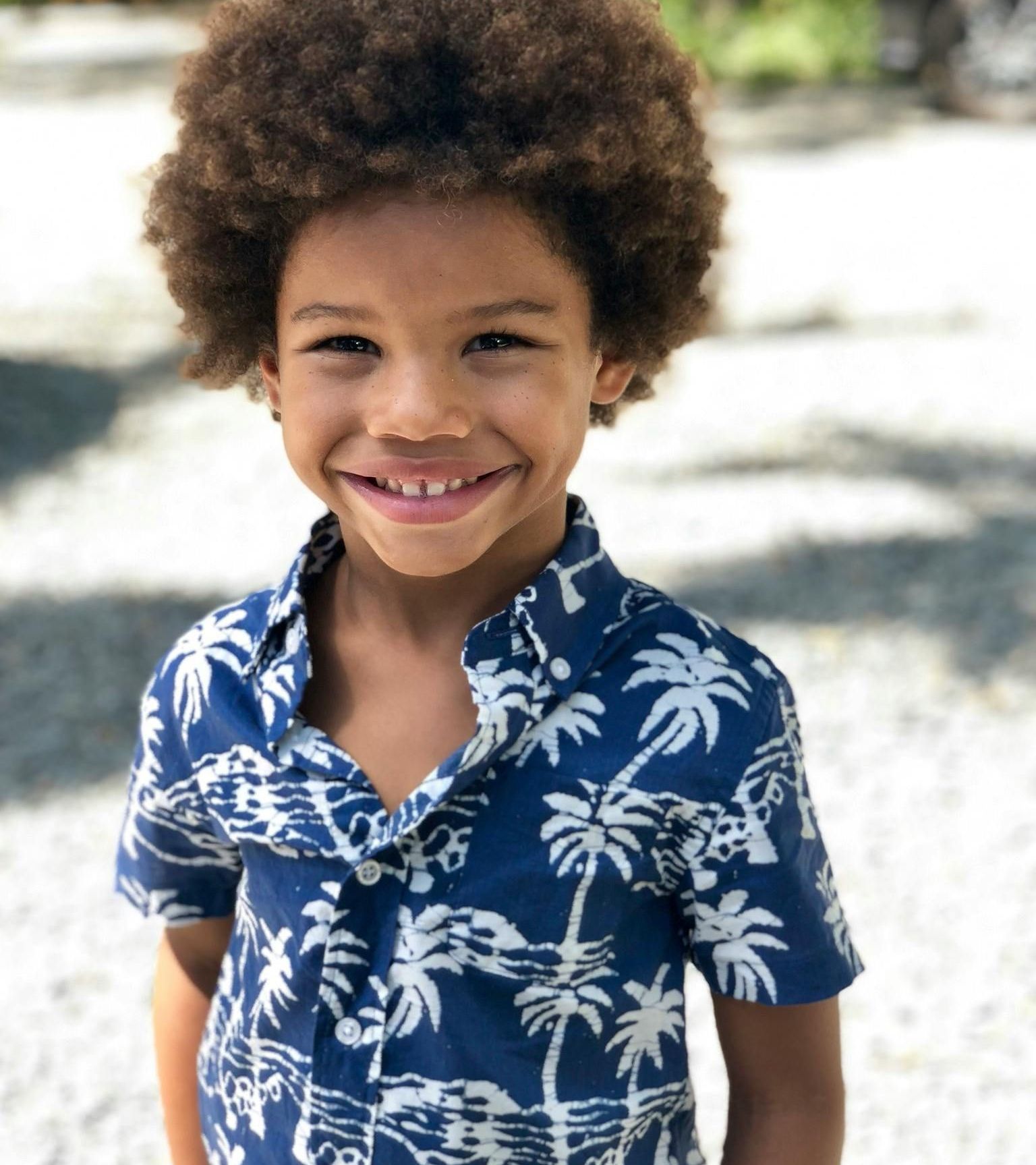 A young boy wearing a blue shirt with palm trees on it