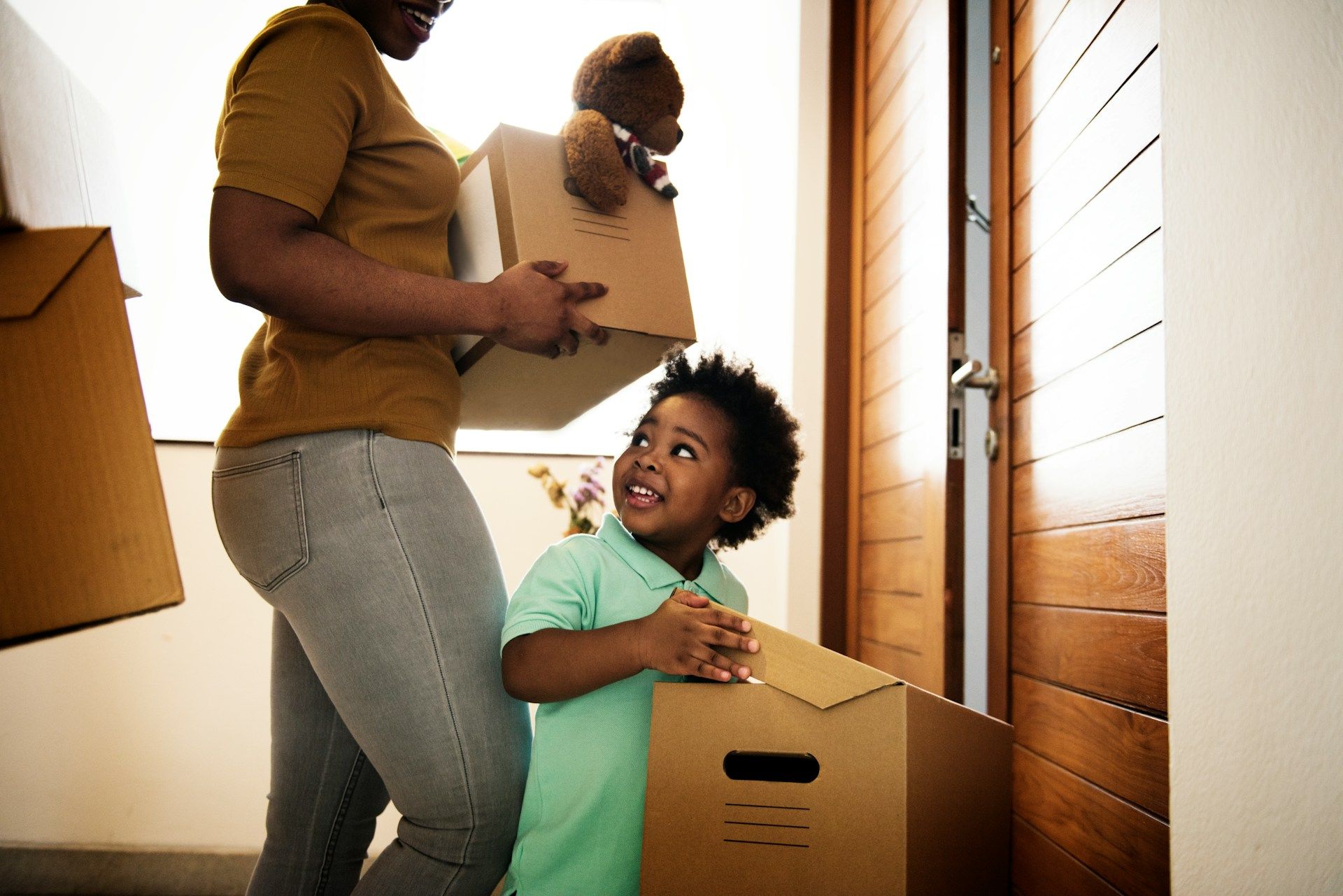 Woman and child carrying moving boxes through doorway.