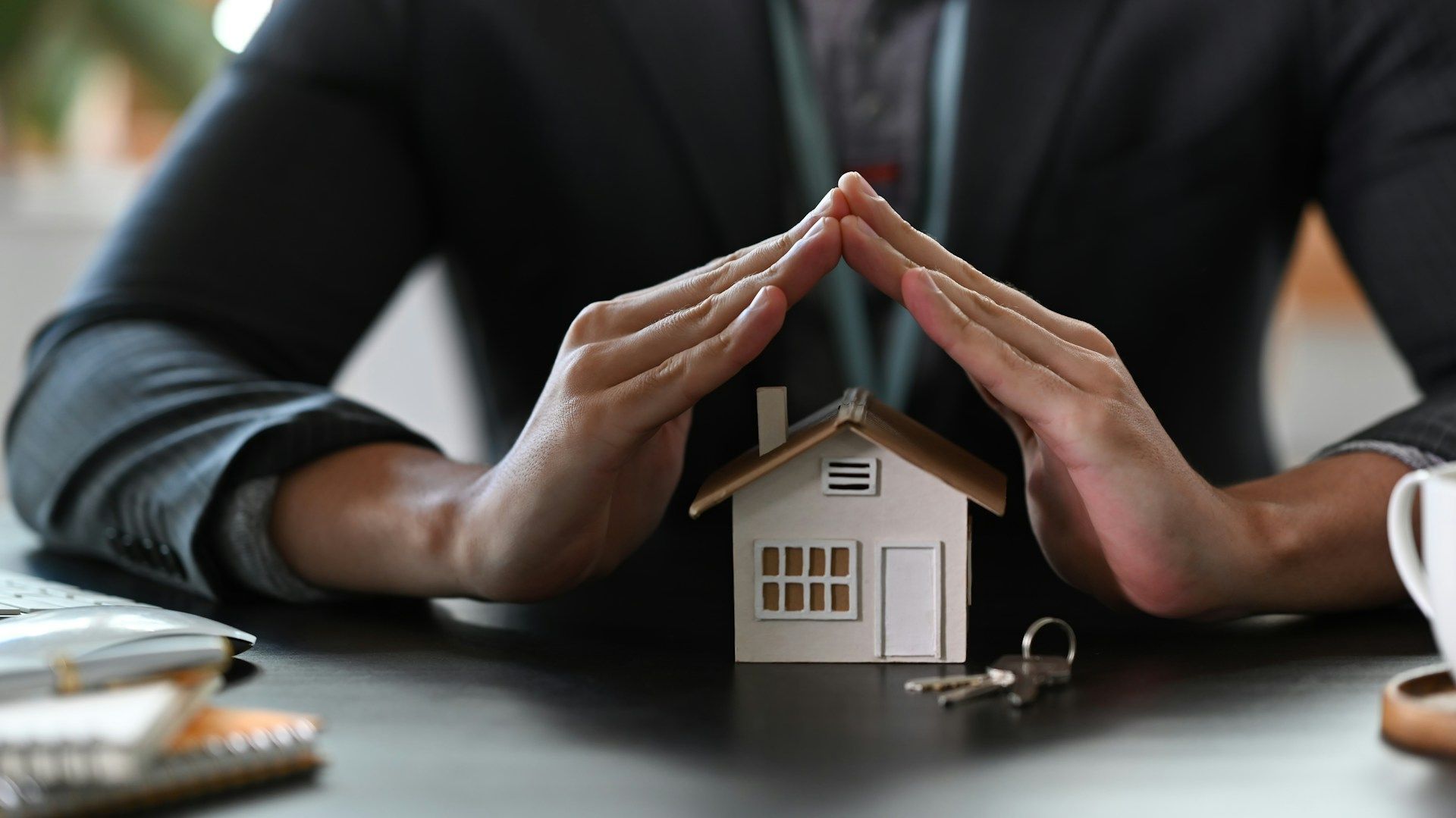 Hands over a model house, symbolizing protection and home insurance.